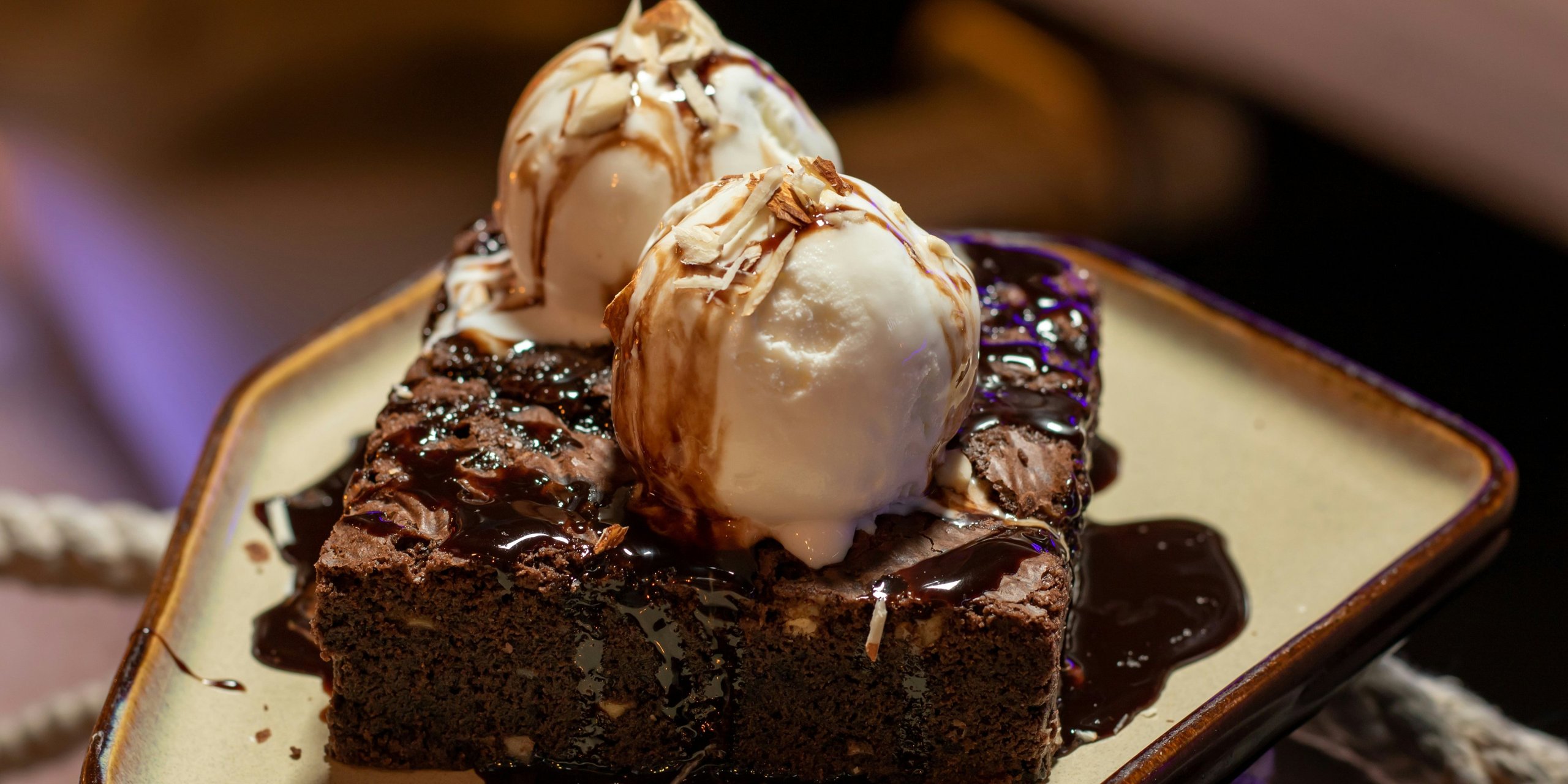 A chocolate brownie under two scoops of vanilla ice cream, chocolate sauce pooling on the plate