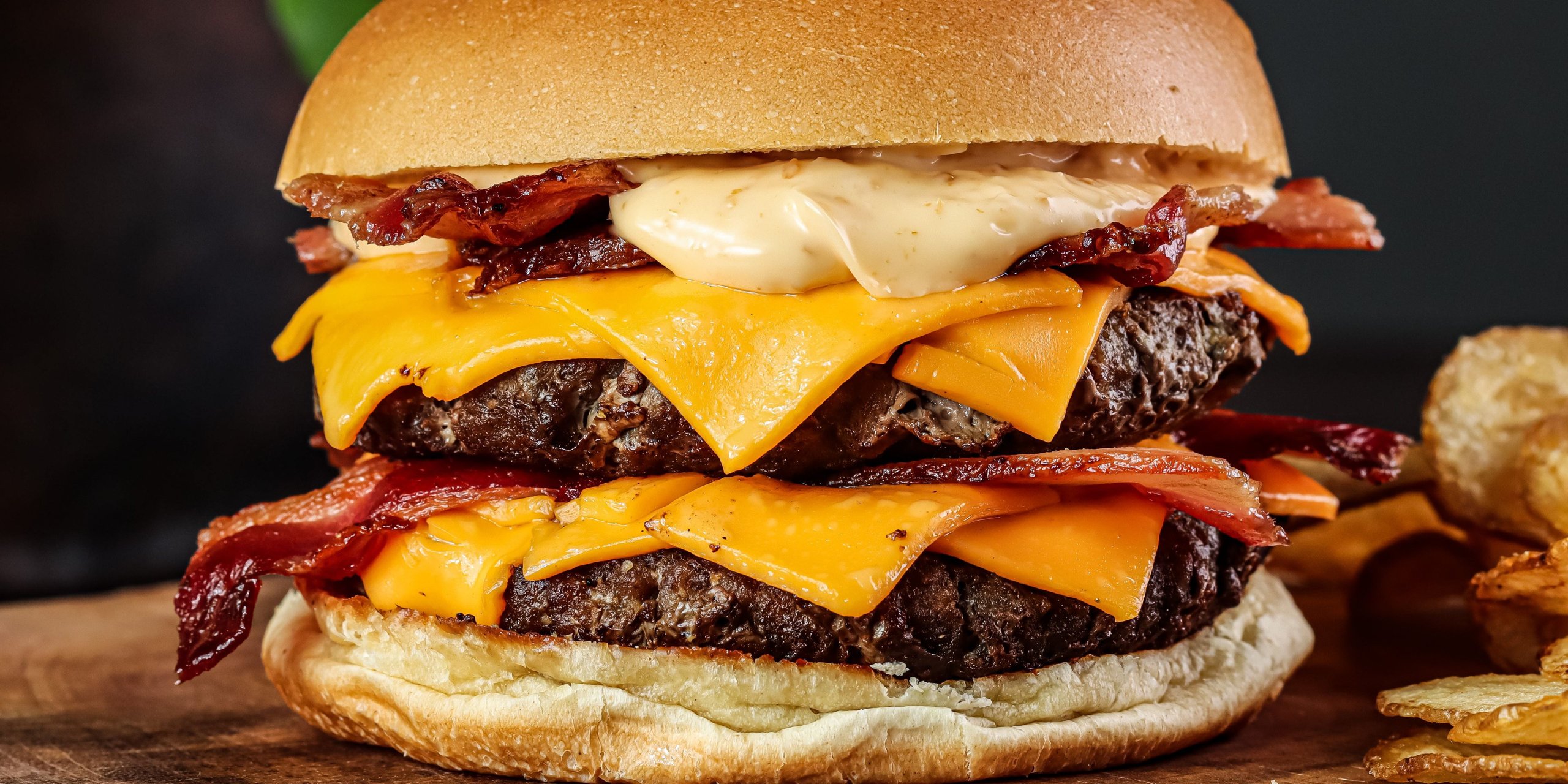 A double beef burger with crisp bacon and melting cheddar on a wooden board